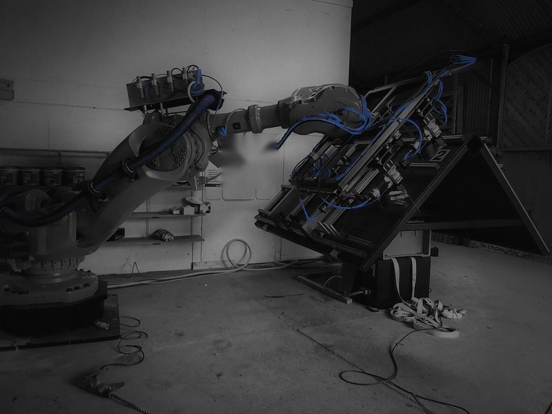Robot holding its end effector at the top edge of the turntable rig, dark-graded