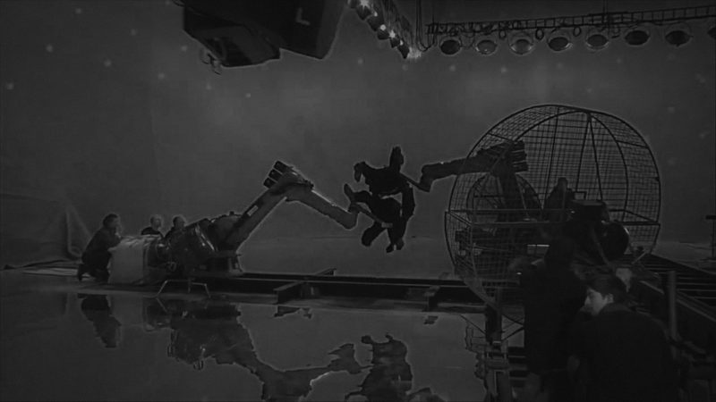 Dual industrial robots on a green-screen stunt set, video still, dark-graded