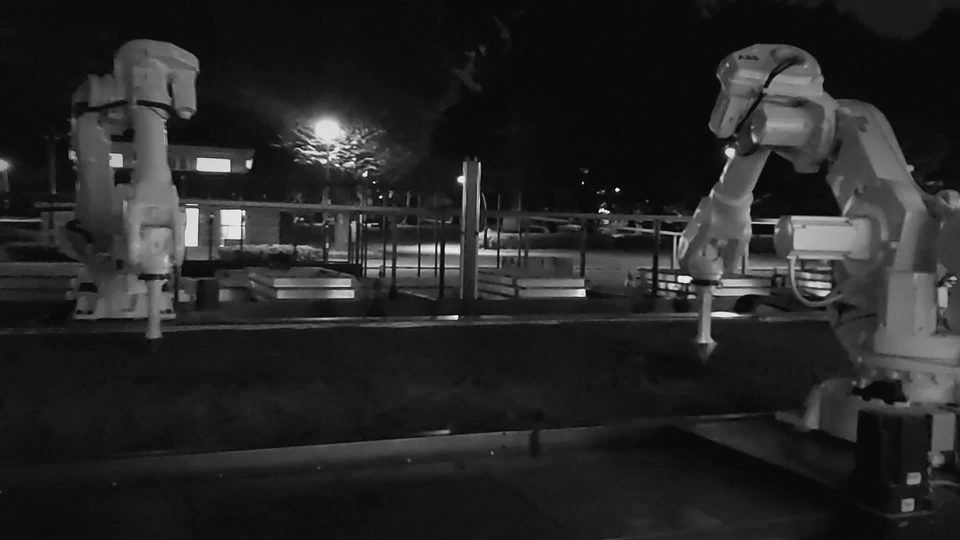 Two white industrial robots working the garden bed at night in Ueno Park, Tokyo, dark-graded video still